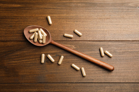 Dietary supplement capsules with spoon on wooden table, flat layの写真素材