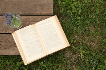 Open book with flowers in glass on green grass outdoors, top view. Space for textの写真素材