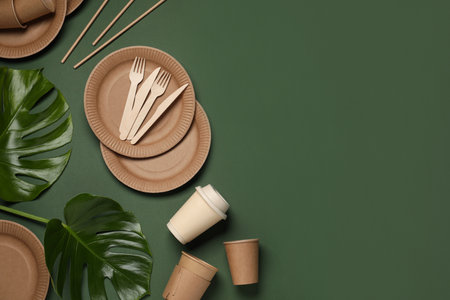 Flat lay composition with disposable tableware and monstera leaves on dark green background. Space for textの写真素材