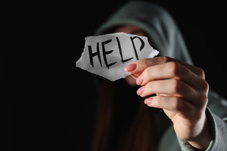 Woman holding piece of paper with word Help on black background, closeup. domestic violence conceptの写真素材