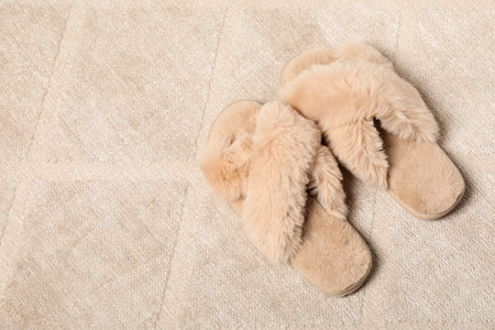 Fluffy beige slippers on soft carpet, space for textの写真素材