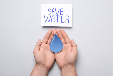 Man holding paper drop near card with words Save Water on light gray background, top viewの写真素材