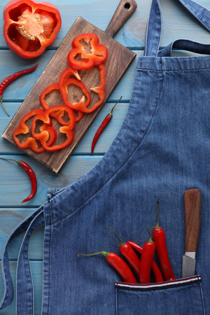 Flat lay composition with denim apron and fresh peppers on light blue wooden tableの写真素材