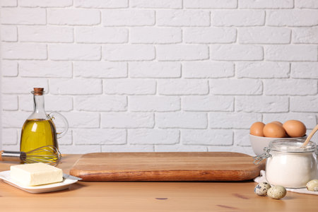 Many different ingredients for dough on wooden table near white brick wall