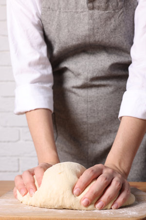 Woman kneading dough at wooden table near white brick wall, closeupの写真素材