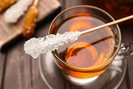 Stick with sugar crystals and cup of tea on wooden table, closeupの写真素材