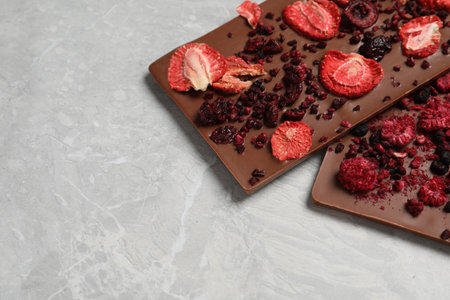 Chocolate bars with freeze dried berries on gray marble table, closeup. Space for text