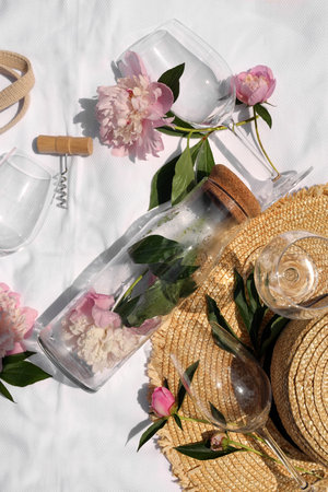 Flat lay composition with beautiful peonies and wineglasses on white fabric