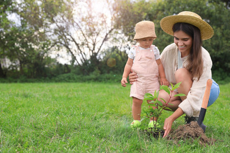 Mother and her baby daughter planting tree together in garden, space for textの写真素材