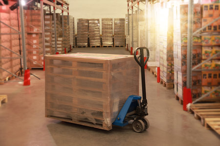 Modern manual forklift with wrapped wooden pallets in warehouseの写真素材