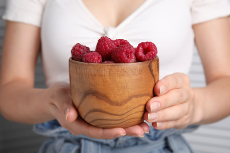 Woman holding wooden bowl of fresh raspberries, closeupの写真素材