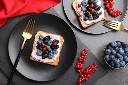 Tasty sandwiches with cream cheese and berries on gray table, flat lay