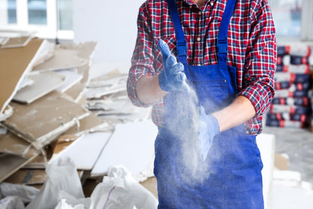 Construction worker shaking off dust from hands in room prepared for renovation, closeupの写真素材