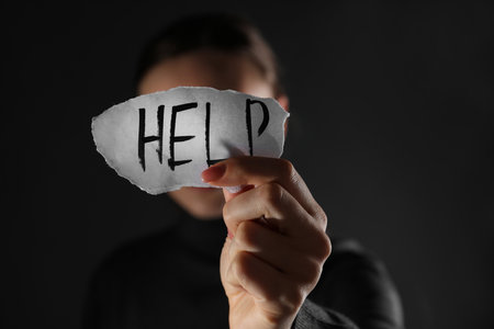 Woman holding piece of paper with word Help on black background, closeup. domestic violence conceptの写真素材