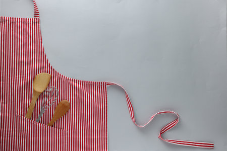 Red striped apron with kitchen tools on light gray background, top view. Space for textの写真素材