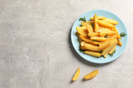 Plate with tasty baked potato wedges and rosemary on gray table, flat lay. Space for textの写真素材