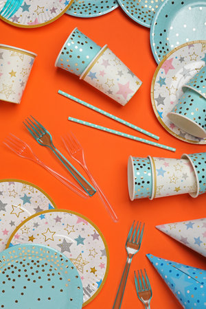 Disposable tableware on orange background, flat lay