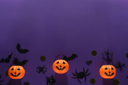 Flat lay composition with plastic pumpkin baskets, paper bats and spiders on purple background, space for text. halloween decorの写真素材