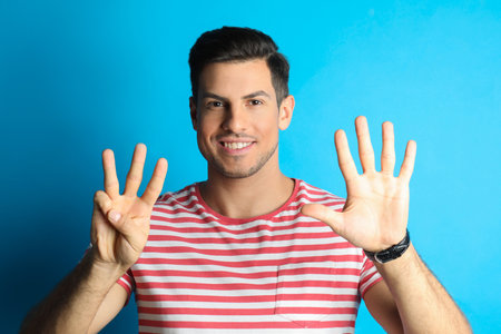 Man showing number eight with his hands on light blue backgroundの写真素材