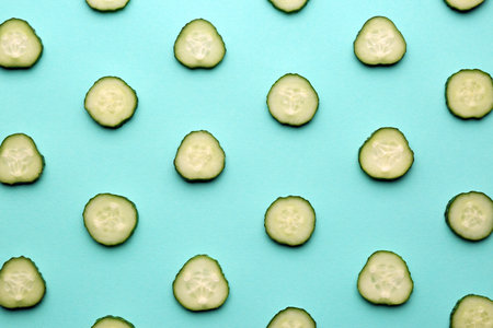 Slices of fresh ripe cucumber on turquoise background, flat layの写真素材
