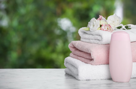 Soft towels, flowers and shower gel bottle on marble table outdoors, closeup. Space for textの写真素材