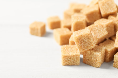 Heap of brown sugar cubes on white table, closeup. Space for textの写真素材