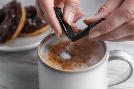 Woman adding sugar to tasty coffee at white wooden table, closeupの写真素材