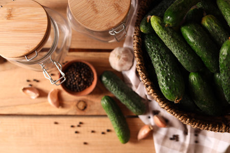 Fresh cucumbers and other ingredients near jars prepared for canning on wooden table, flat layの写真素材