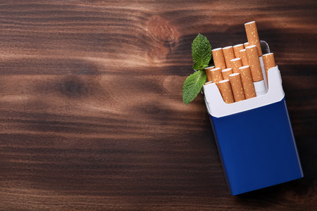 Pack of menthol cigarettes and mint leaves on wooden table, flat lay. Space for textの写真素材