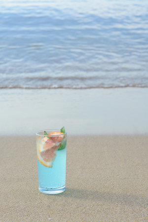 Glass of refreshing drink with grapefruit and mint on sandy beach near sea, space for textの写真素材
