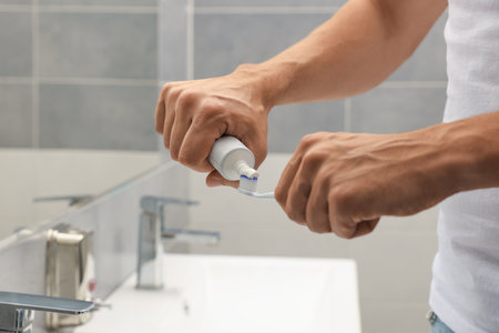 Man applying toothpaste on brush in bathroom, closeupの写真素材