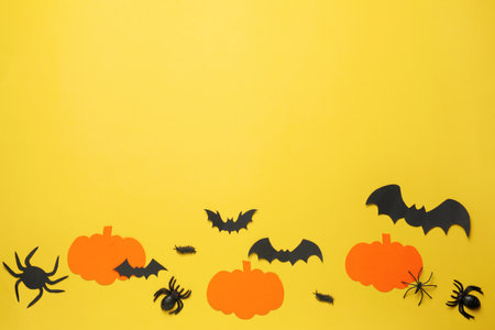 Flat lay composition with paper pumpkins, bats and spiders on pale yellow background, space for text. halloween celebrationの写真素材