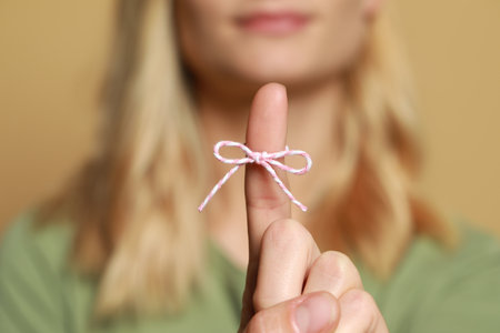 Woman showing index finger with tied bow as reminder against light brown background, focus on handの写真素材