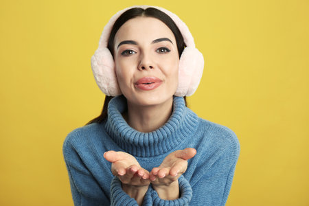 Beautiful young woman wearing earmuffs on yellow backgroundの写真素材
