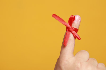Man showing index finger with red tied bow as reminder on orange background, closeup. Space for textの写真素材