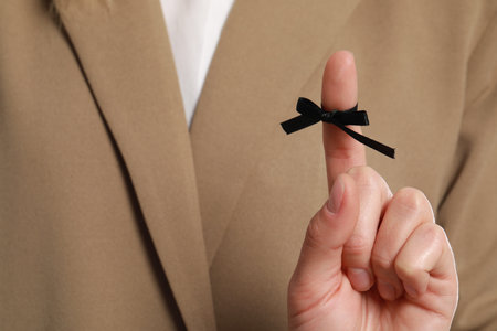 Woman in beige suit showing index finger with tied black bow as reminder, closeupの写真素材