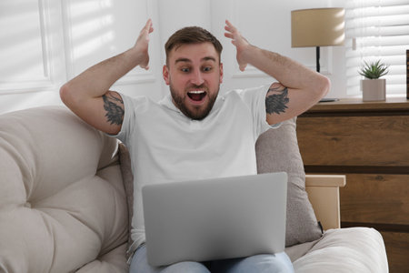 Emotional man participating in online auction using laptop at home