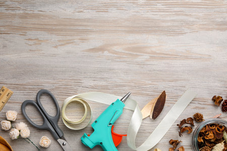 Hot glue gun and handicraft materials on white wooden table, flat lay. Space for text
