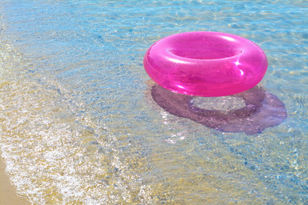Bright inflatable ring on sandy beach near sea. Space for textの写真素材