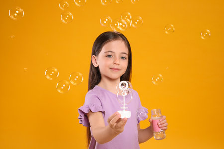 Little girl having fun with soap bubbles on yellow backgroundの写真素材
