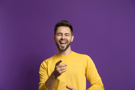 Young man laughing on purple background. funny jokeの写真素材