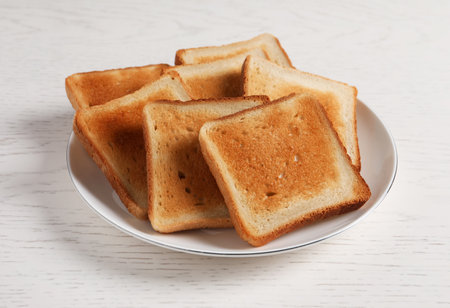 Plate with slices of delicious toasted bread on white wooden tableの写真素材