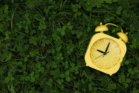 Yellow alarm clock on green grass outdoors, top view. Space for text