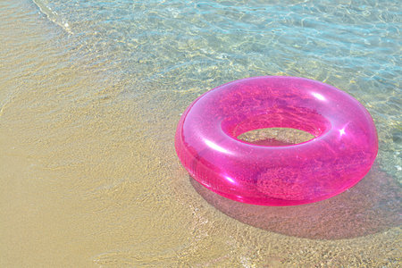 Bright inflatable ring on sandy beach near sea. Space for textの写真素材