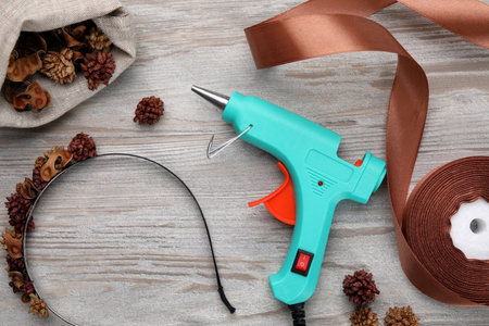 Hot glue gun, decorated headband and handicraft materials on wooden table, flat layの写真素材
