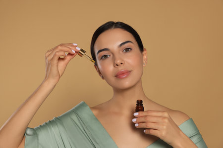 Young woman applying essential oil onto face against beige backgroundの写真素材