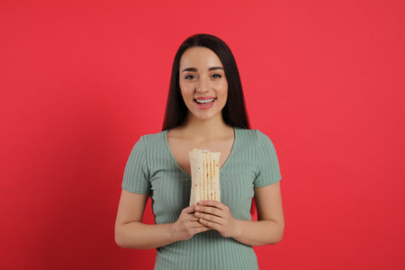 Happy young woman holding tasty shawarma on red backgroundの写真素材