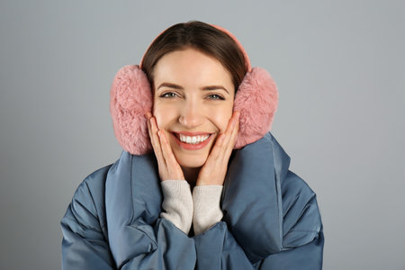 Happy woman wearing warm earmuffs on gray background