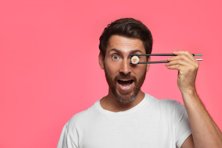 Funny man hiding his eye with tasty sushi roll on pink background. Space for textの写真素材