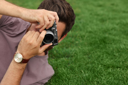 Man with camera taking photo on green grass, space for text. interesting hobby